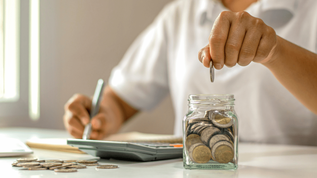 A person putting coins in a jar on a table