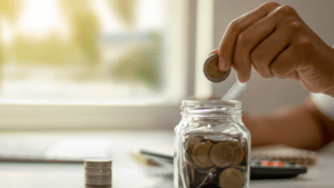 A person putting coins in a jar on a table