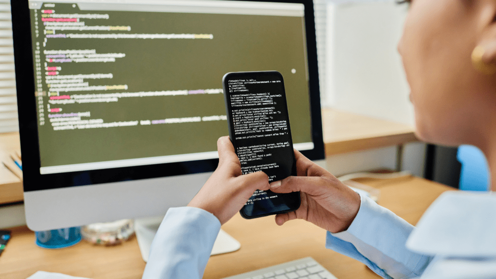 a person is holding a smartphone in front of a laptop with code on the screen