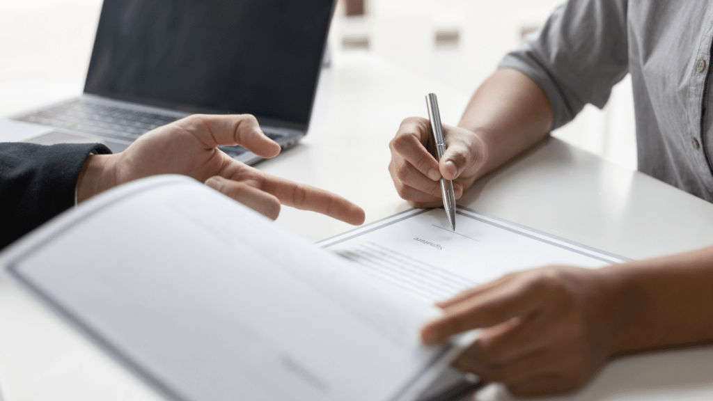 a person in a suit is signing a contract on a piece of paper