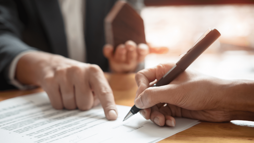 a person signing a contract with a pen and paper on a wooden table